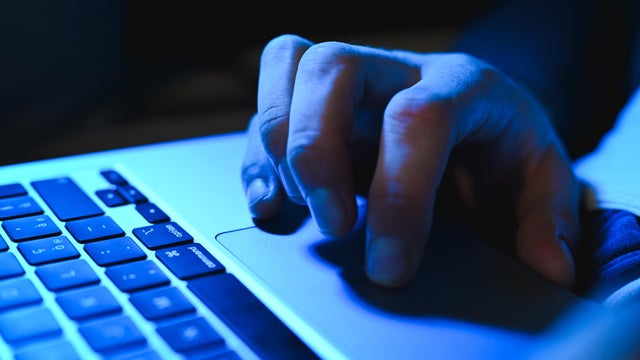 Close up of hacker hand typing on laptop keyboard in dark room 