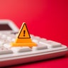 Yellow warning sign on white calculator with red background copy space. 