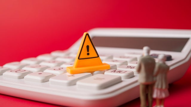 Senior couple looking at yellow warning sign on white calculator with red background. 