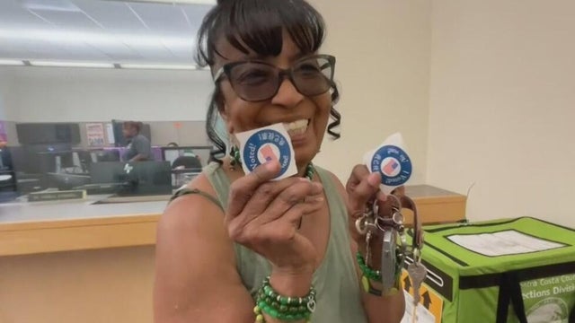 a woman holds two I voted stickers 