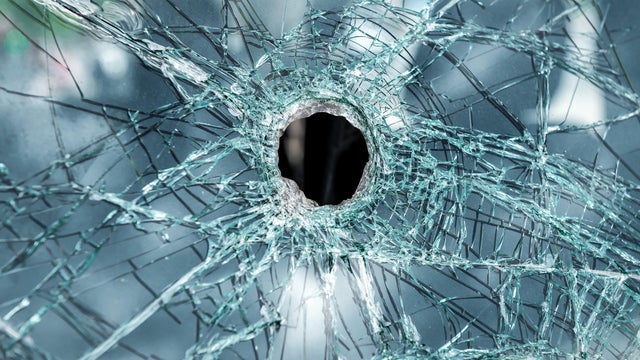 Bullet hole in broken windshield glass 