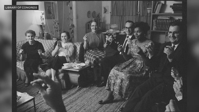 An archival black and white image of the Myers family and others in a living room 