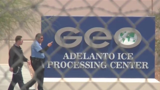 Two men seen walking behind a chainlink fence in front of a federal immigration processing center 