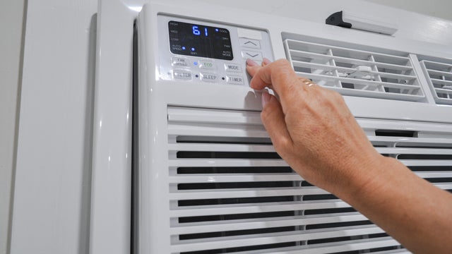 Woman's hand adjusting temperature on modern air conditioner unit 