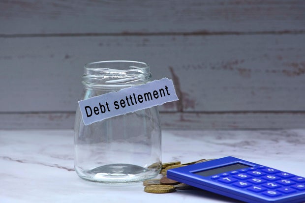 Glass jars with blurred multicurrency coins, calculator and text on white torn paper - Debt settlement 