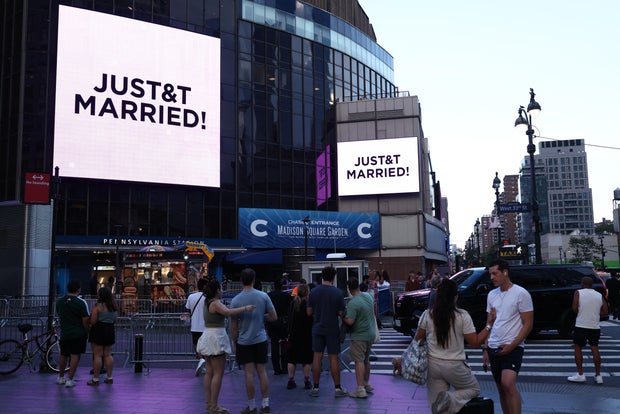 People watch giant screens showing the message "JUST&T MARRIED!" (T&T for Taylor and Travis) outside Madison Square Garden, the venue for the wedding celebrations of pop singer Taylor Swift and pro-athlete Travis Kelce, in New York City on July 3, 2026. 
