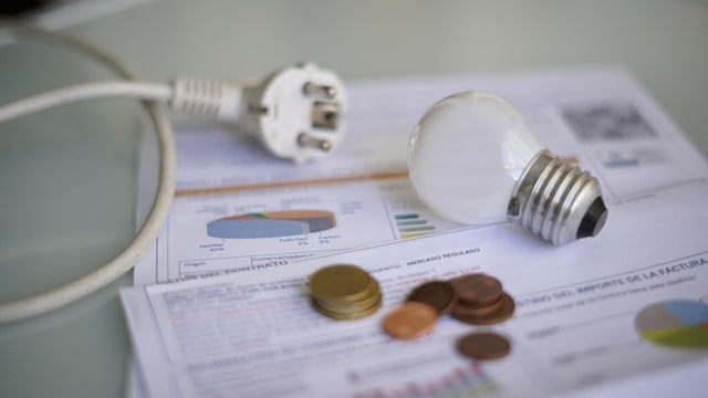 An electricity bill on a table with a cable and plug, a light bulb, and coins 