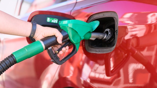 Close-up of a woman standing at a gas station filling her car with gasoline. 