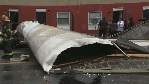 A warped section of roof is seen on the ground, residents and firefighters are standing nearby