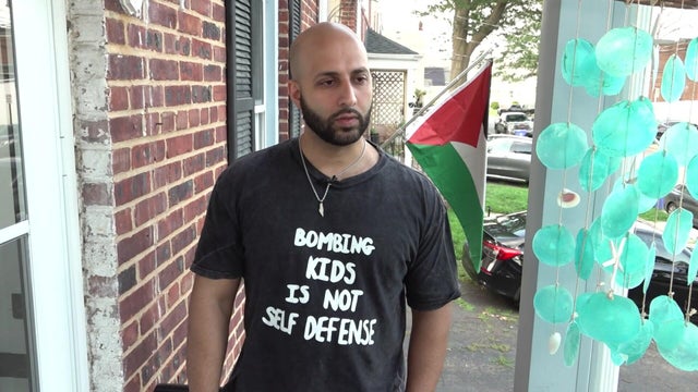Man wearing "bombing kids is not self defense" t-shirt with Palestinian flag in background 