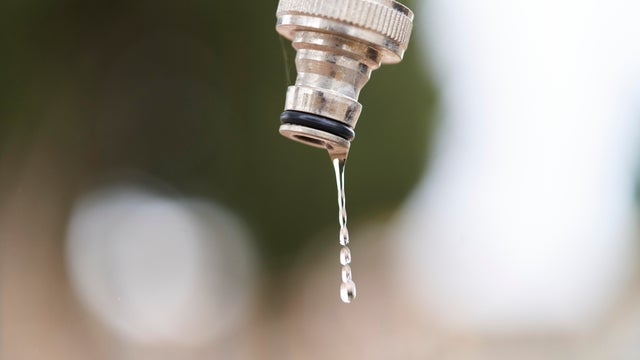 close-up of a drop falling from drinking water faucet, blurred background in open air 