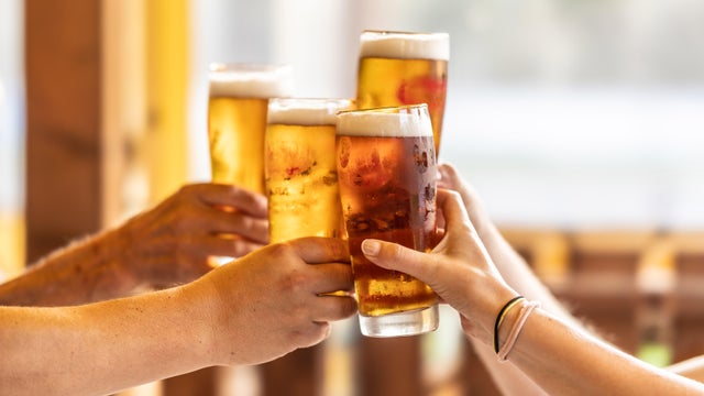 Group of friends toasting with beer on the terrace during hot summer days. Close-up of a group of people clinking glasses with beer. 