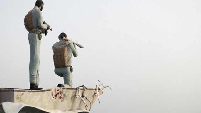 FILE PHOTO: A statue of Iranian military members stands as vessels in the Strait of Hormuz are visible near the beach of Bandar Abbas 