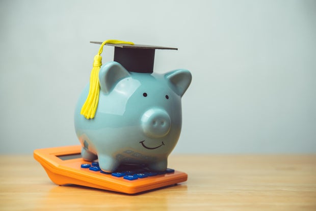 Piggy bank wear mortarboard and orange calculator on wooden table white wall background copy space. 