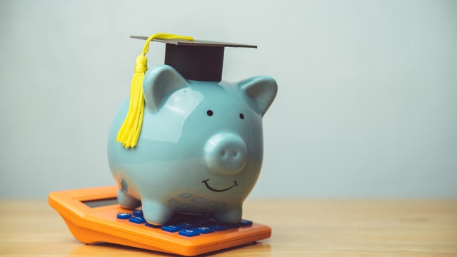 Piggy bank wear mortarboard and orange calculator on wooden table white wall background copy space. 