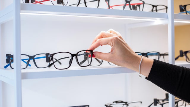 Hand of unrecognizable woman reaches out to touch pair of eyeglasses lying on display 