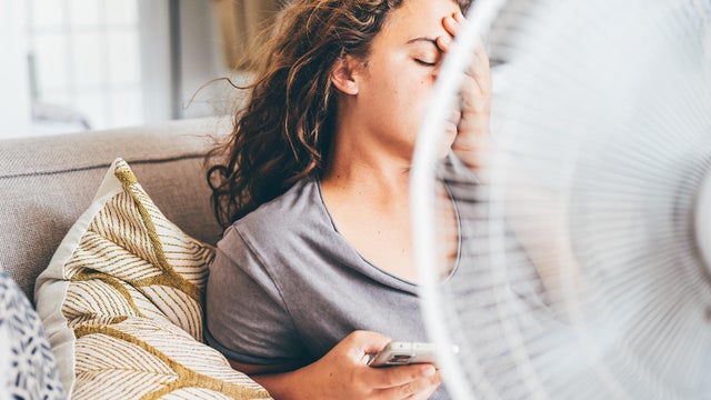 Happy contented woman using electric fan at home enjoying fresh air on hot summer day. 