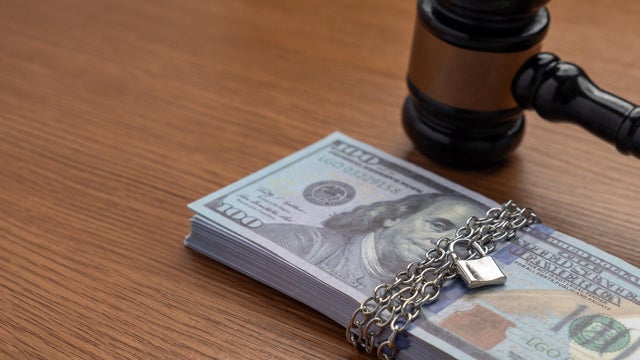 A judge's gavel next to a stack of money bound by a metal chain and secured with a padlock. 