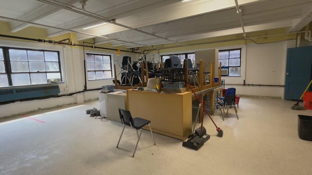Classroom items stacked up in the middle of a room that was damaged in flooding 