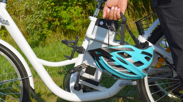 Women with helmet stand near electric bicycle in the park in sunny summer day. The view of the e bike battery pack. Unfiltered, with natural lighting. 