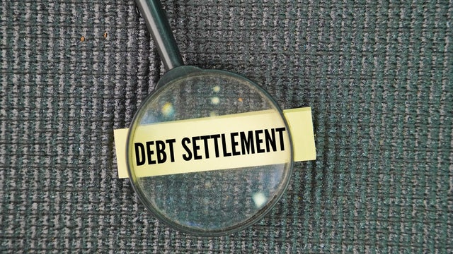 Magnifying glass and paper with the word debt settlement. 