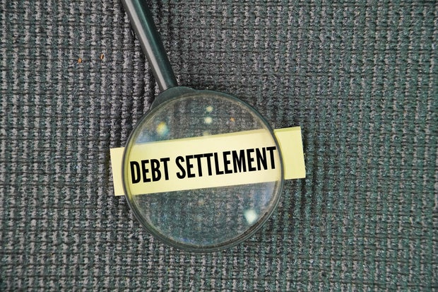 Magnifying glass and paper with the word debt settlement.