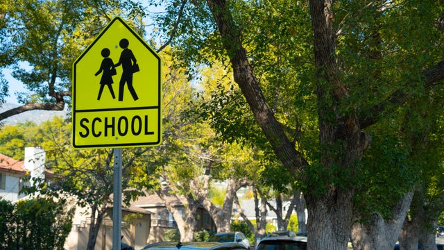 Bright yellow school crossing sign with children silhouette and text 'SCHOOL' on a sunny day 