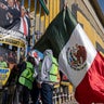 Demonstrators hang a Mexican flag alongside protest banners and crosses on the U.S. border wall in Playas de Tijuana, Baja California state, Mexico on Dec. 18, 2025. 