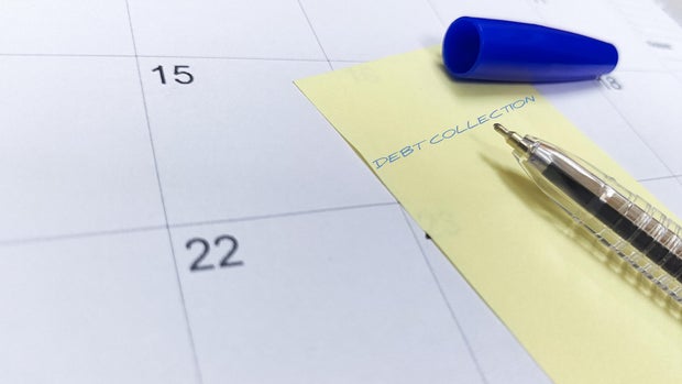 A pen and sticky note labeled "Debt Collection" rest on a calendar, highlighting an upcoming payment deadline.