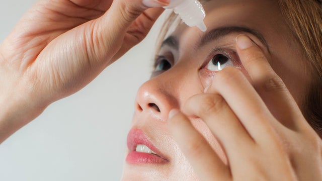 A young woman is applying medicine drops on her eyes 