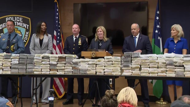 Officials speaking behind a table filled with bricks of cocaine.