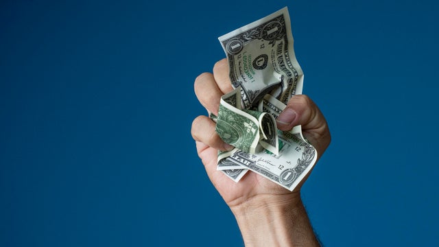 Hand Clenching Crumpled US Dollar Bills Against Blue Background 