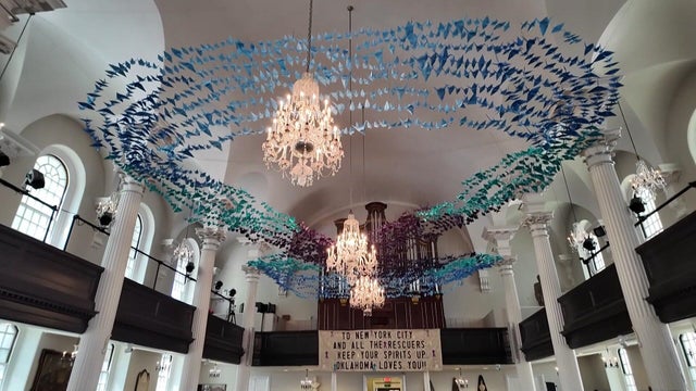 Hundreds of blue paper cranes hung in the shape of an infinity symbol from the ceiling of a church 