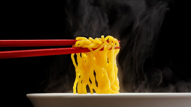Sapporo ramen noodle lifted up by red chopsticks with steam against black background 
