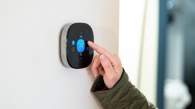 woman adjusting temperature on digital thermostat 