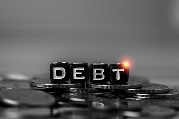 Debt concept with letter blocks on stacked coins in monochrome tone. Financial crisis, loan repayment, credit risk, bankruptcy, economic downturn and personal finance problem background.