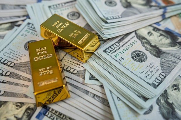 Shiny gold bullion bars on hundred dollar banknotes representing luxury, savings and financial stability 