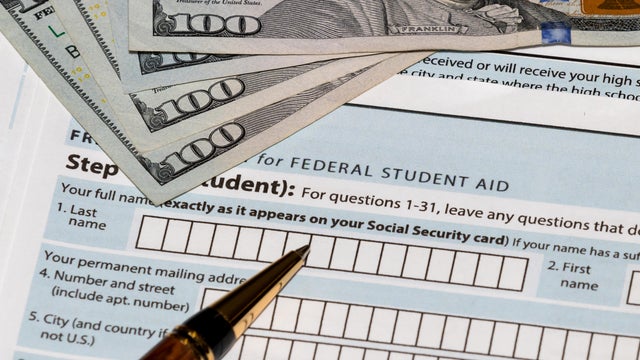 Student financial aid application forms for college tuition loans and grants with one-hundred dollar bills and ballpoint pen 
