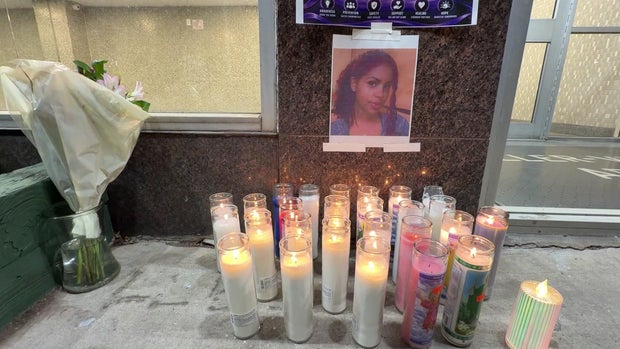 A photo of Nathaly Ramirez taped to the exterior wall of a building with prayer candles