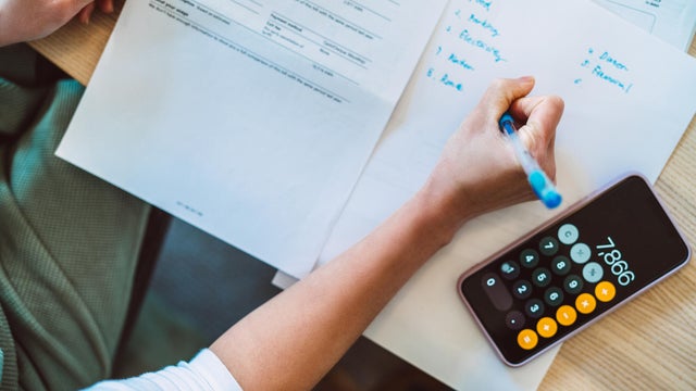 Overhead view of young Asian women managing home finance using smartphone. She is working with household utility bill and  calculating expenses at home. 